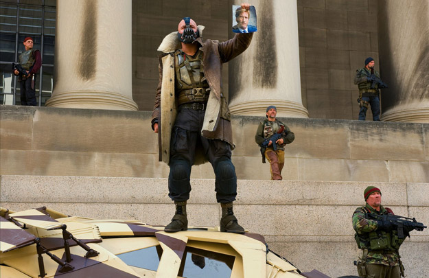 Bane y su grupo de terroristas se ríen del caballero blanco de Gotham... el fallecido Harvey Dent